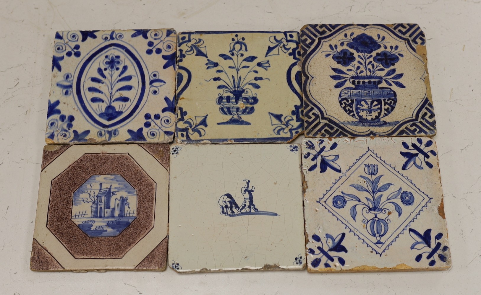 Four mid 17th century Delft blue and white ‘urn of flowers’ tiles, and an 18th century Delft ‘acrobats’ tile and blue and manganese ‘landscape’ tile (6)